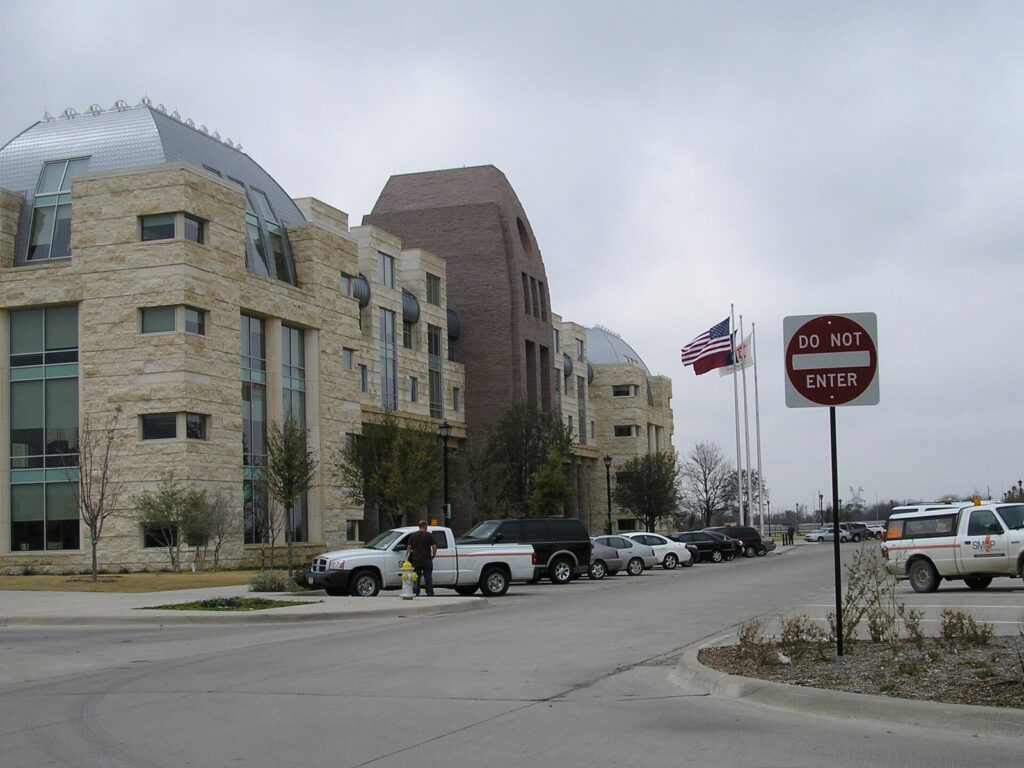Stone and glass Frisco City Hall building with flags beside a parking lot