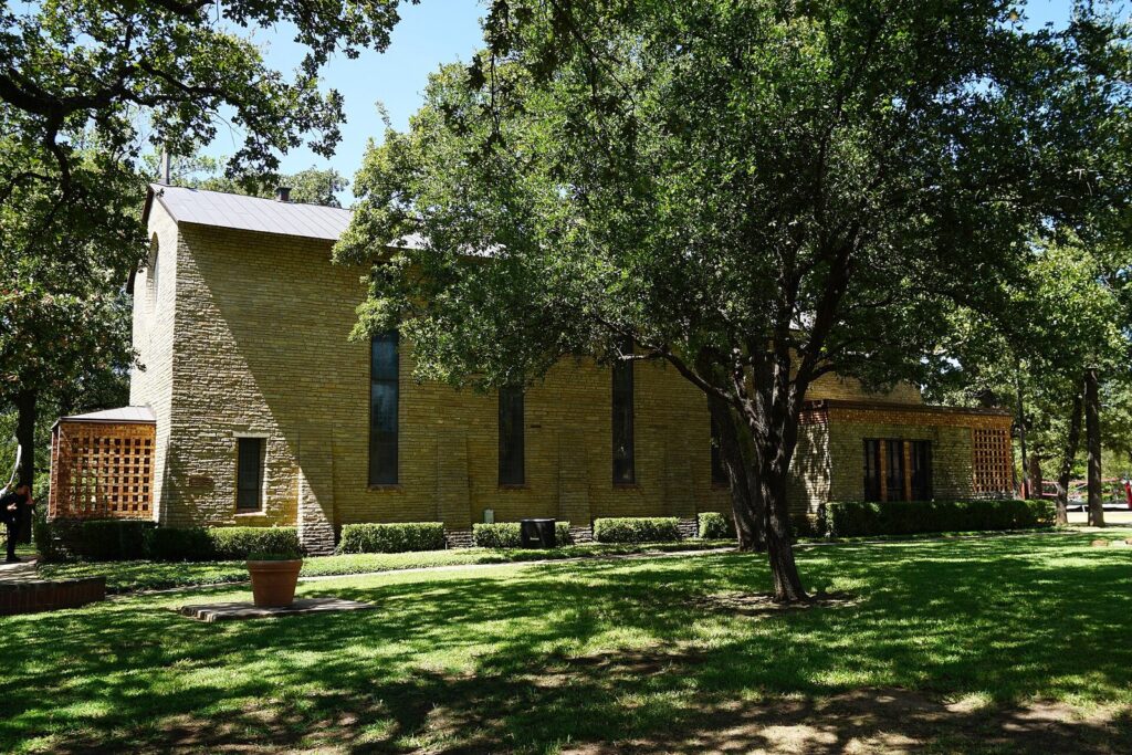 Stone walls and tall windows of the Little Chapel-in-the-Woods under oak trees at Texas Woman's University