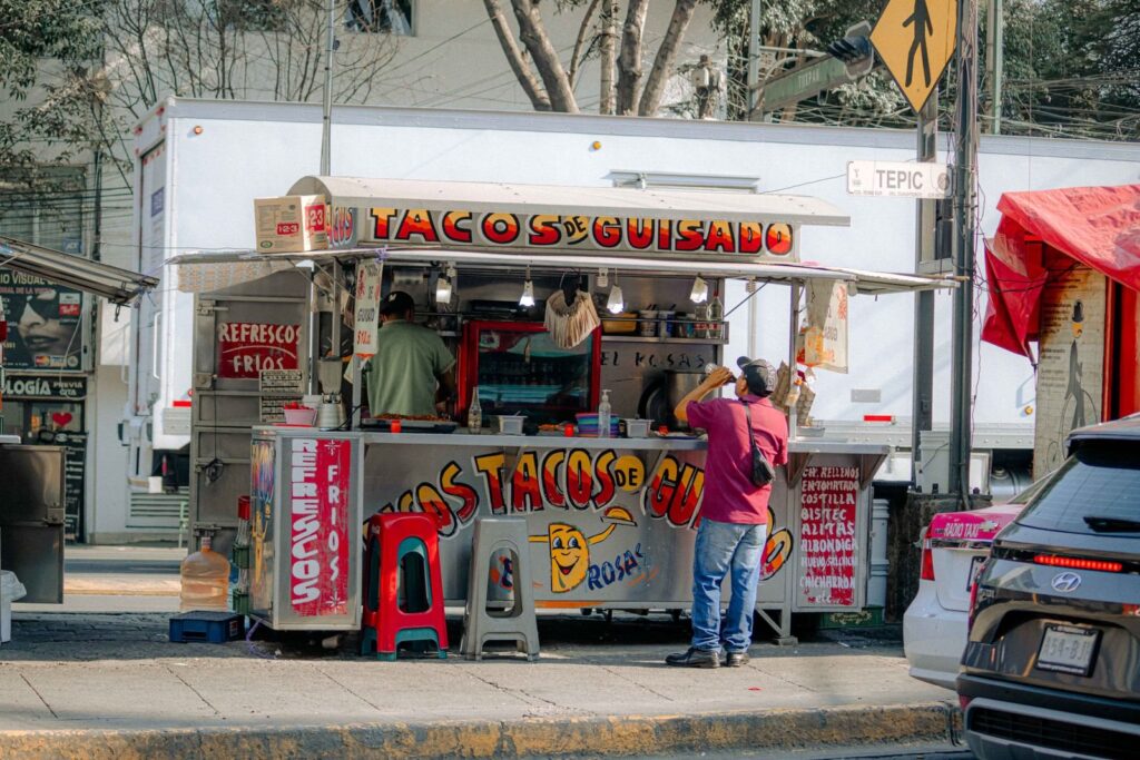 Taco truck with a hand-painted sign and customers ordering on a sidewalk