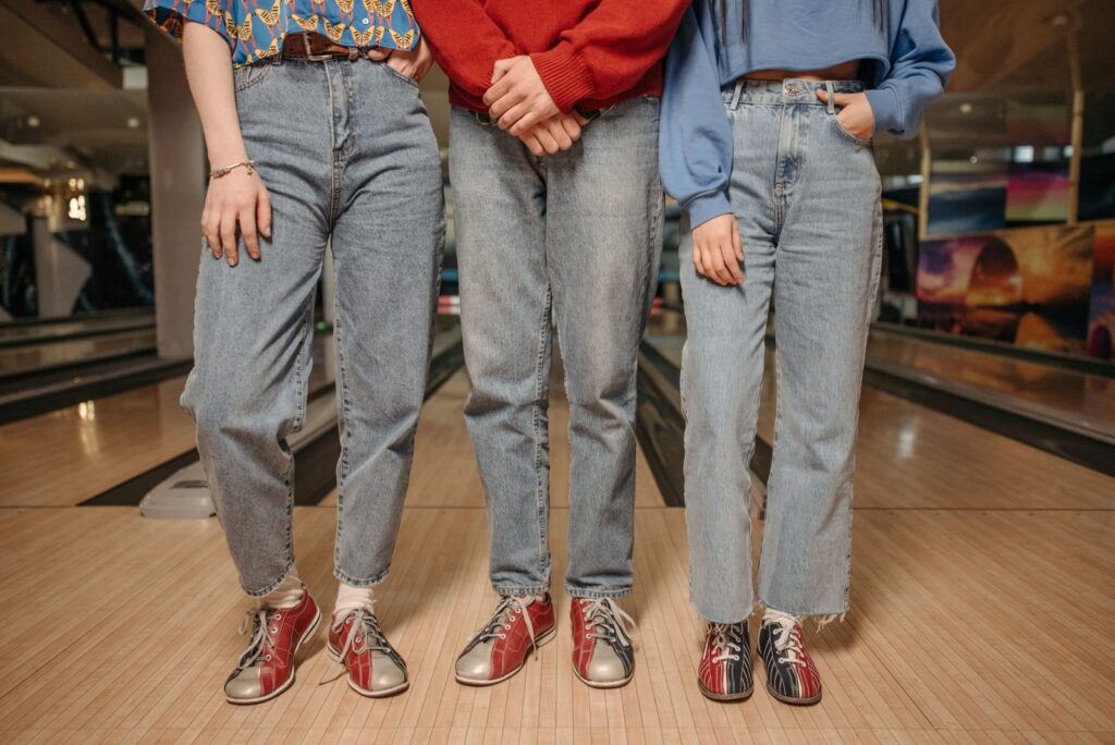 Three friends in jeans and two-tone rental bowling shoes standing on the approach