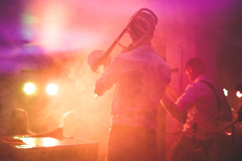 Trombone player and bandmates performing on a hazy stage under warm pink and orange lights