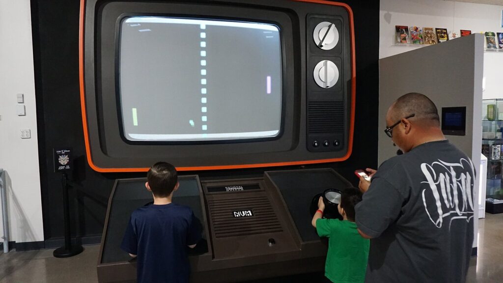 Two children and an adult playing Giant Pong on an oversized retro TV cabinet