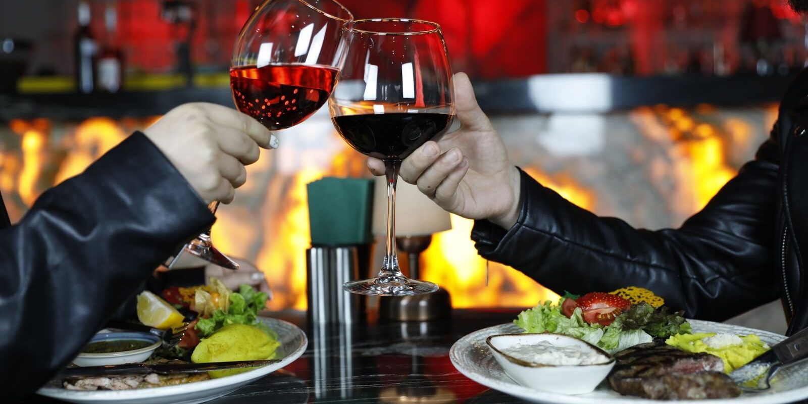 Two glasses of red wine raised over steak and seafood plates for date night in Frisco TX