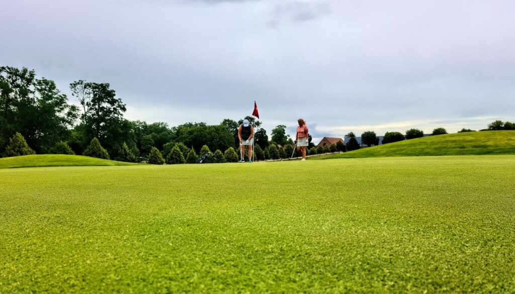 Two golfers on a putting green at a grass course under a cloudy sky