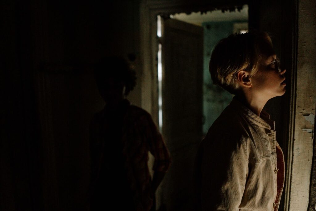Two people peer through a doorway into a dark, abandoned-looking room