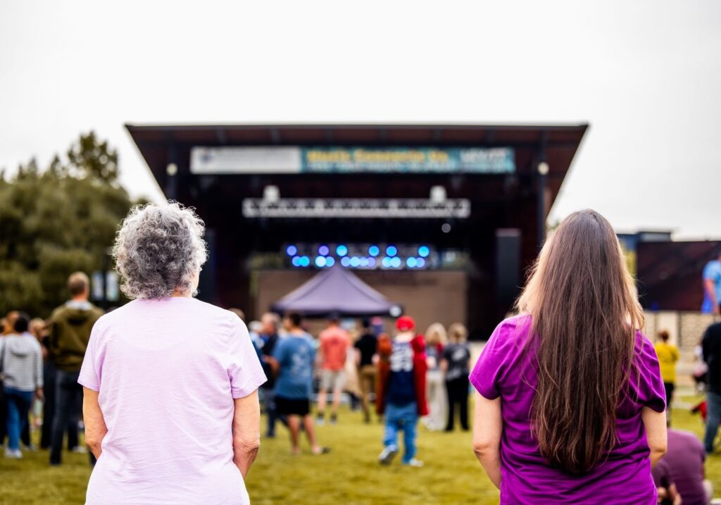 Two women watching a festival stage from the lawn at an outdoor concert