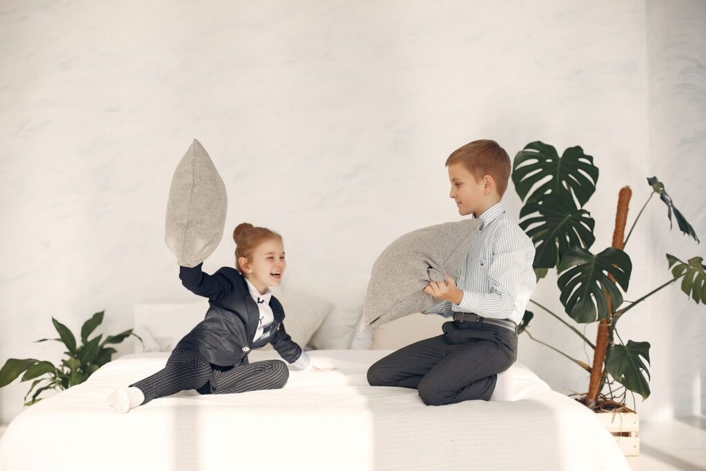 Two young children playing with pillows on a hotel bed