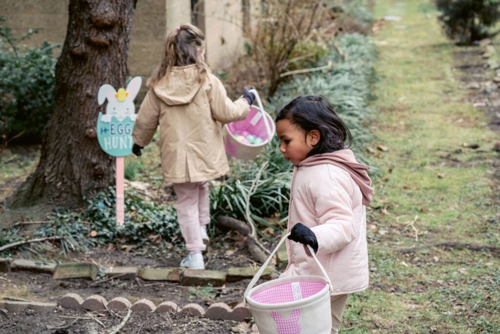 Two young girls carrying baskets and searching for eggs at an outdoor Easter egg hunt