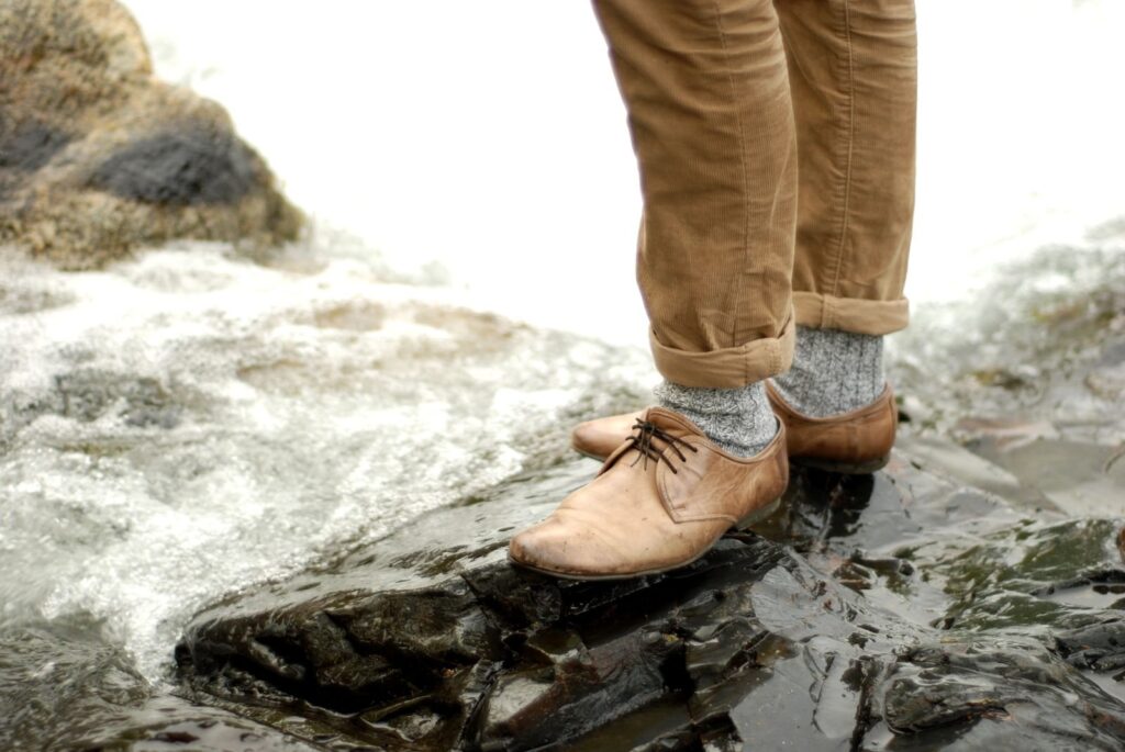Walker in lace-up leather shoes standing on a wet rock beside rushing water