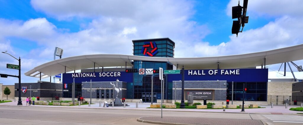 Wide street view of the Hall of Fame building at the south end of Toyota Stadium under a blue sky