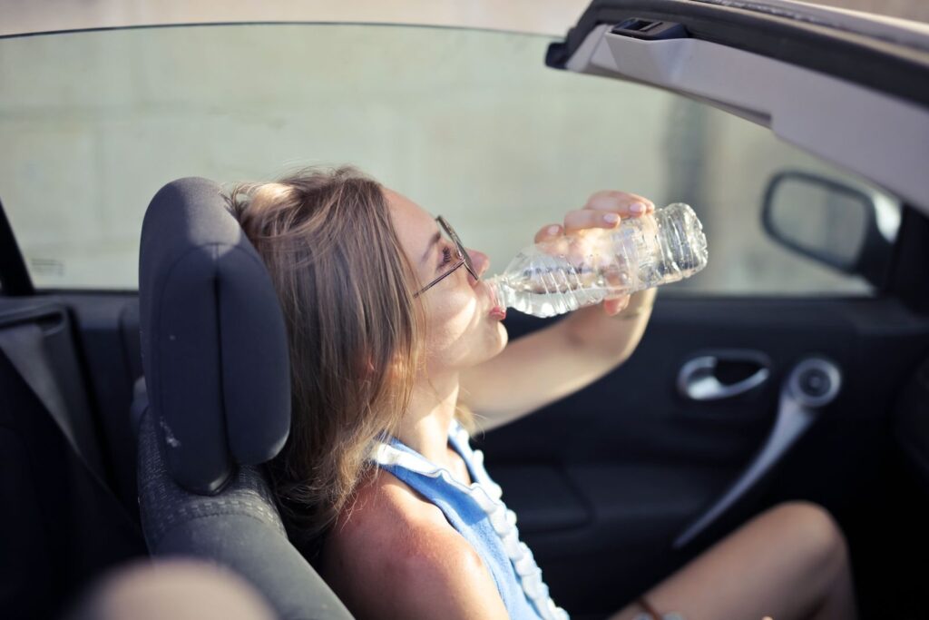 Woman drinking bottled water while sitting in a convertible car