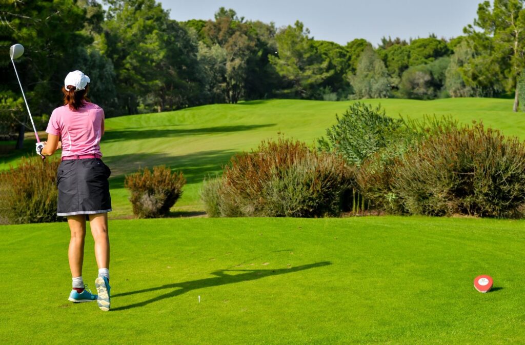 Woman in a pink top and cap holding her finish on a tree-lined golf course