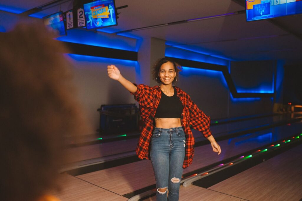 Woman in a plaid shirt celebrating a strike under blue lane lights