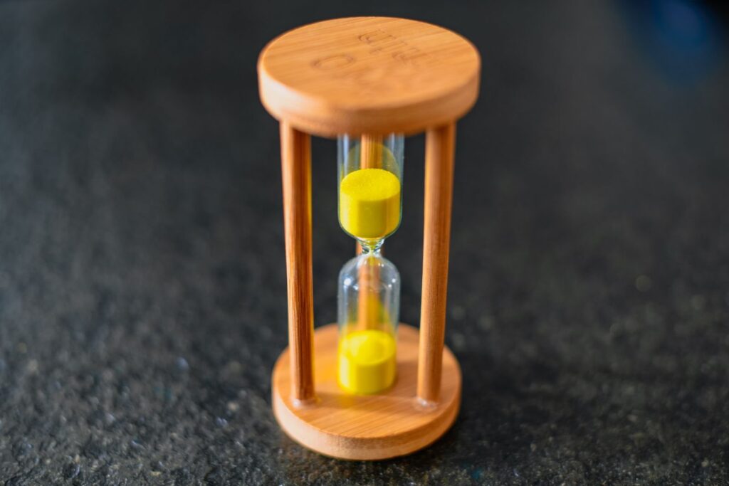 Wooden hourglass with yellow sand running through it on a dark surface