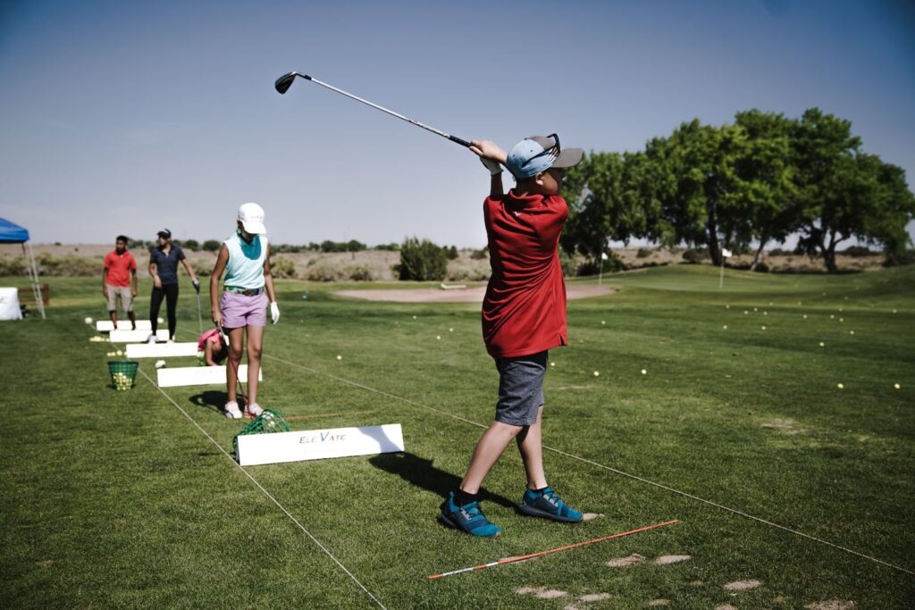 Young golfers swinging at a driving range during an outdoor junior clinic